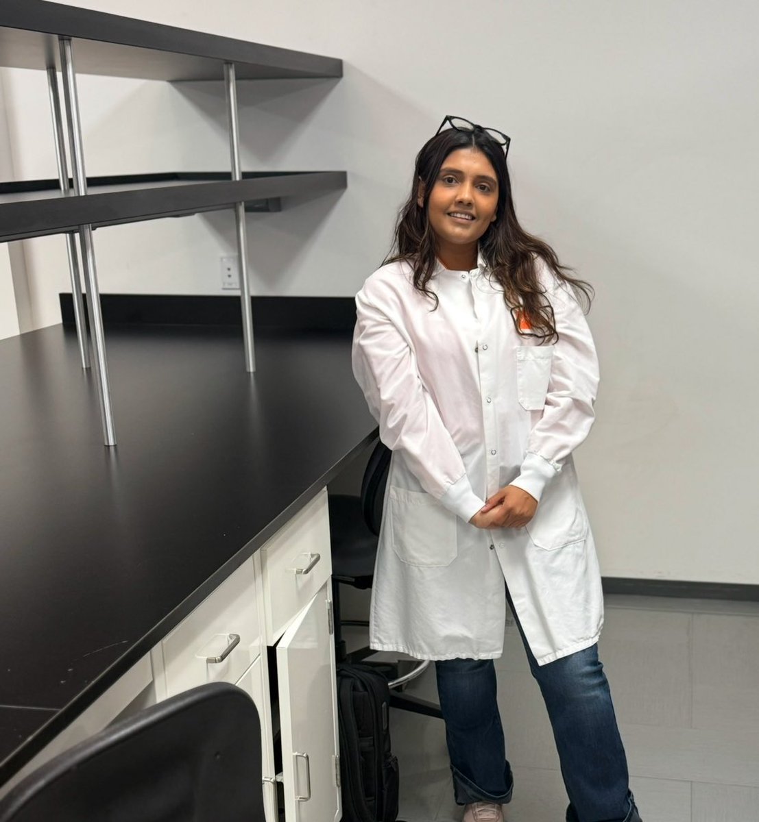 Parmita in a lab coat beside the empty bench in the newly secured lab, February 2025.