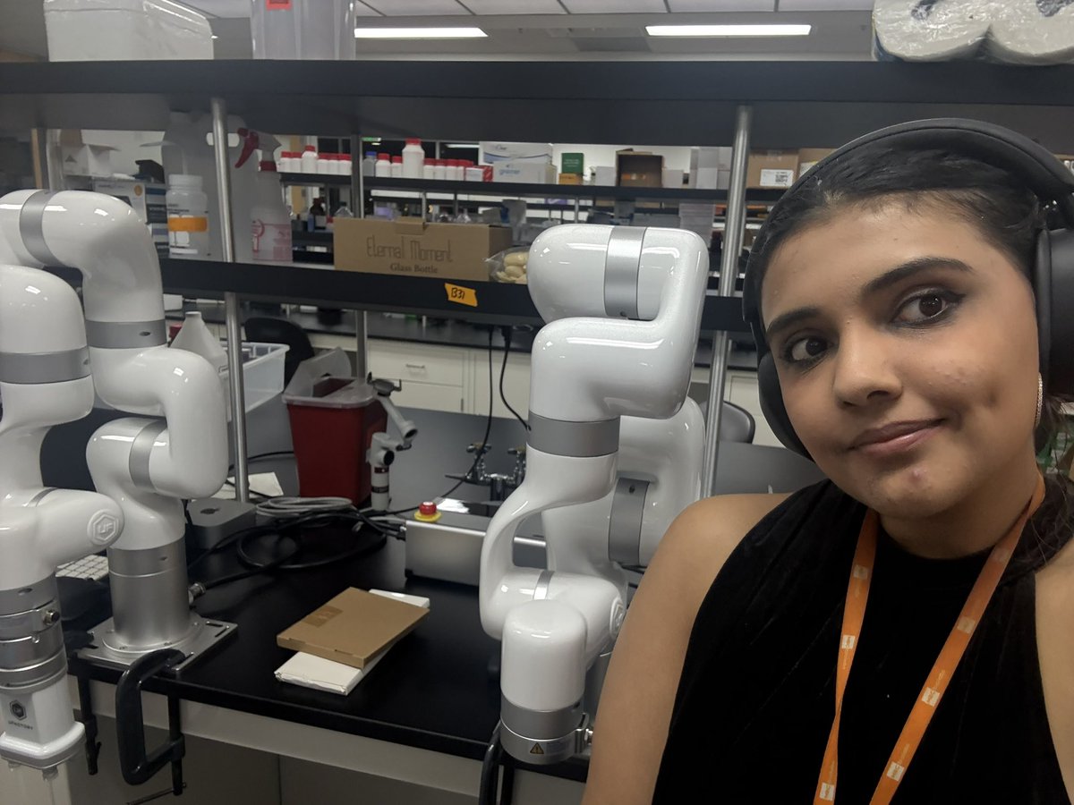 Parmita beside two mounted commercial robot arms on the laboratory bench in June 2025.