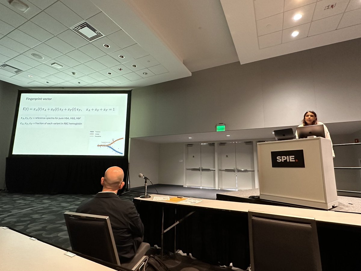 Parmita presenting a Fingerprint vector slide from a SPIE podium, with an audience in the foreground.
